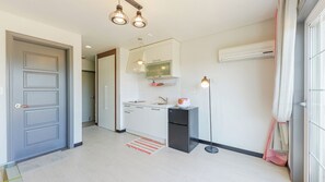 Una cocina moderna con horno empotrado, un lavabo y un refrigerador. Hay una ventana con cortinas y un equipo de aire acondicionado en la pared.