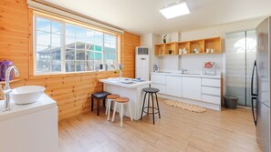 Eine moderne Küche mit großem Fenster, Holzwänden, einer weißen Spüle, Barhocker, einem Kühlschrank und einer Küchenzeile mit Küchenutensilien.