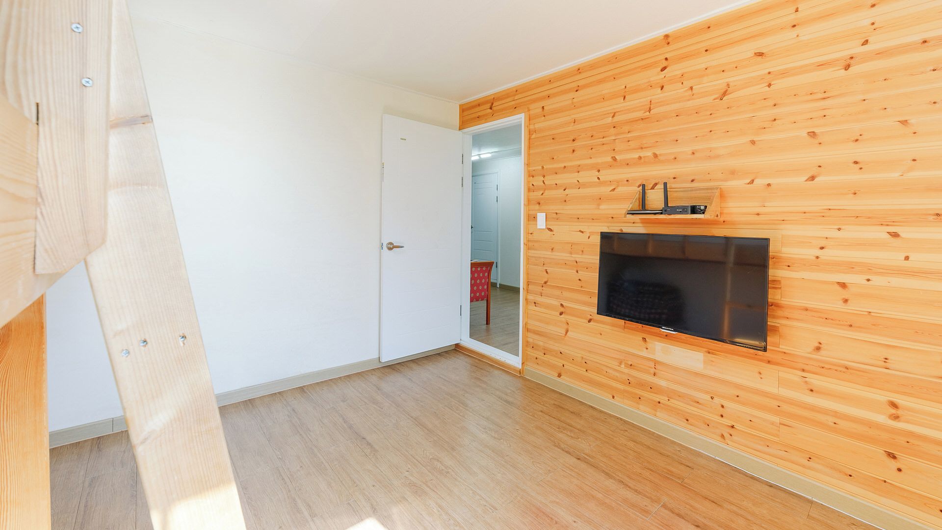 Ein Zimmer mit Holzwandverkleidung, einer weißen Tür, einem an der Wand montierten Flachbildfernseher und einem Holzboden.