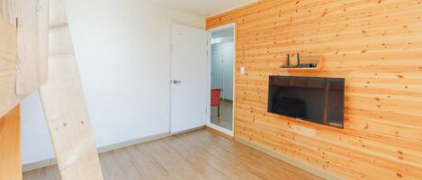 Ein Zimmer mit Holzwandverkleidung, einer weißen Tür, einem an der Wand montierten Flachbildfernseher und einem Holzboden.
