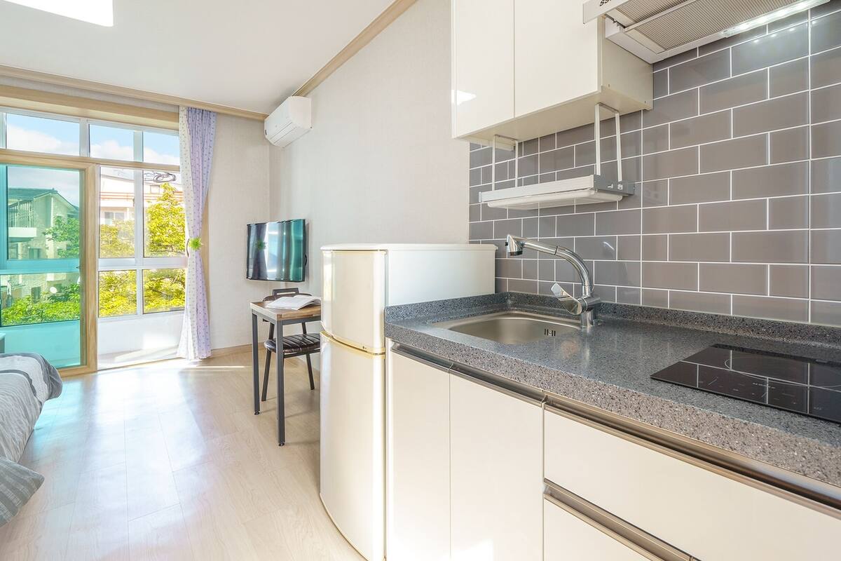 Et moderne køkken med indbygget ovn, vask og et vindue med udsigt til en balkon.