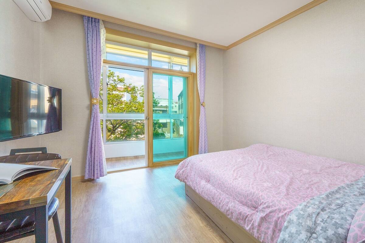 Et soveværelse med seng, skrivebord, fjernsyn og en skydedør til en balkon.