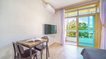 Habitación de hotel con una mesa de madera, dos sillas, un televisor de pantalla plana y un balcón con vistas a árboles.