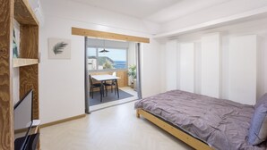 Een slaapkamer met een bed, een bureau en uitzicht op zee door een schuifdeur.