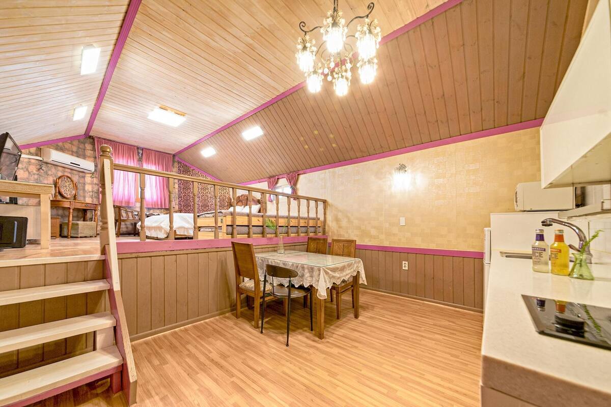 A cozy attic dining area with a wooden table and chairs, a chandelier, and a view of the upper floor.