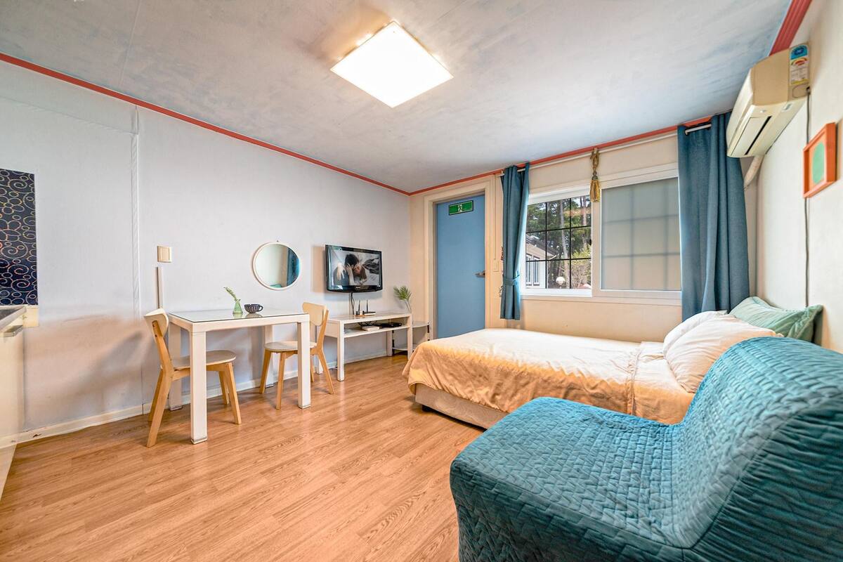 A hotel room with a bed, a desk, a chair, a TV, and a window with curtains.