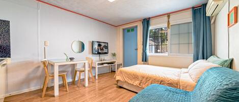 Una habitación de hotel con cama, escritorio, silla, televisor y ventana con cortinas.
