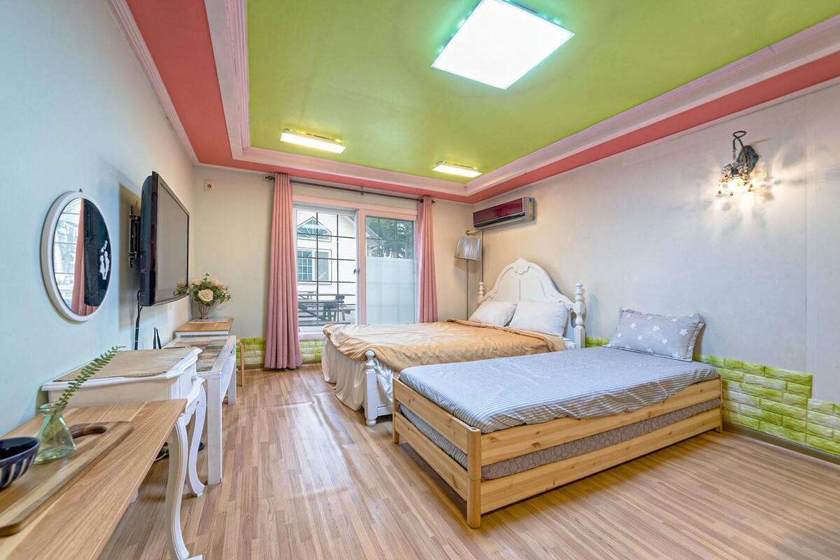 A bedroom with a wooden bed, a desk, a chair, a mirror, and a window with curtains.