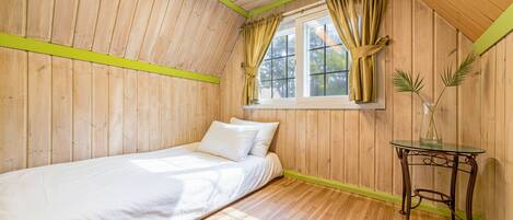 Una cama individual en una habitación con paredes de madera y techo inclinado.