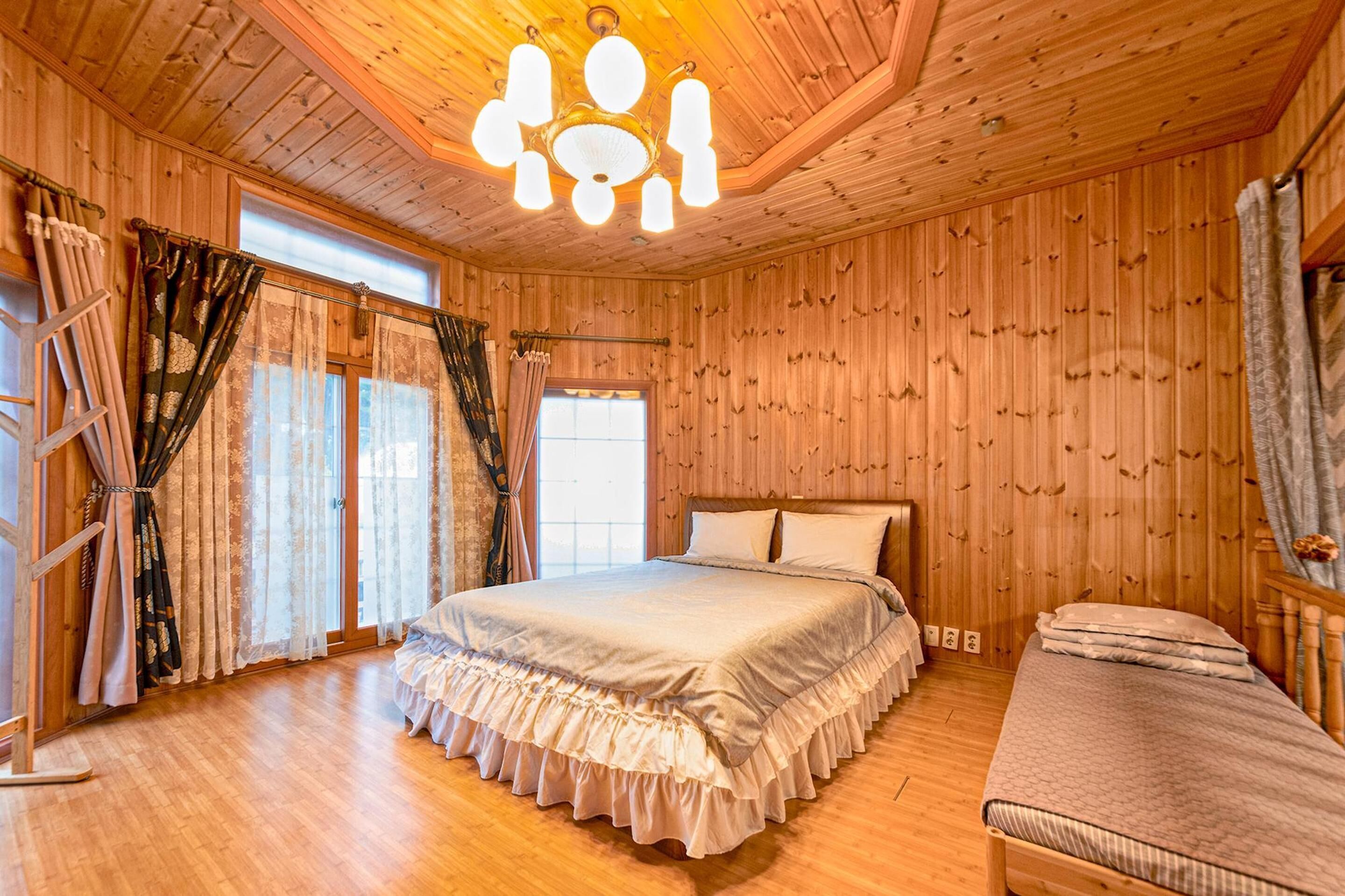 Una habitación con paneles de madera, una cama, un banco y una araña.