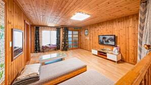 A wooden-paneled room with a television, a sofa, and a glass table. - Gangnueng Gadunji Pension (Gangneung)