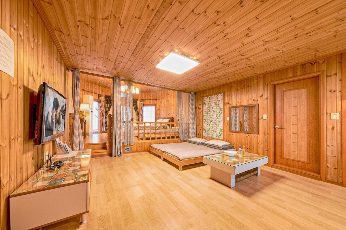 A wooden cabin interior with a bed, a desk, and a bathroom.