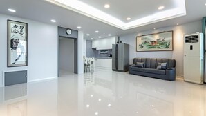 A modern living room with a grey sofa, a dining area with a white table and chairs, a kitchen with white cabinets, and a large framed artwork on the wall. - Gangneung Badauibyeol Pension (Gangneung)