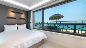 A bedroom with a large bed, a view of the sea, and a wooden deck with a table and umbrella. - Gangneung Badauibyeol Pension (Gangneung)