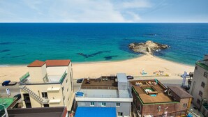 A beach with clear blue waters and a rocky outcrop in the center. There are buildings with balconies overlooking the beach. - Gangneung Badauibyeol Pension (Gangneung)