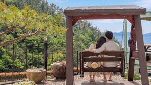 Ein Paar sitzt auf einer Holzbank unter einer Holzpergola mit Blick auf eine gebirgige Landschaft.