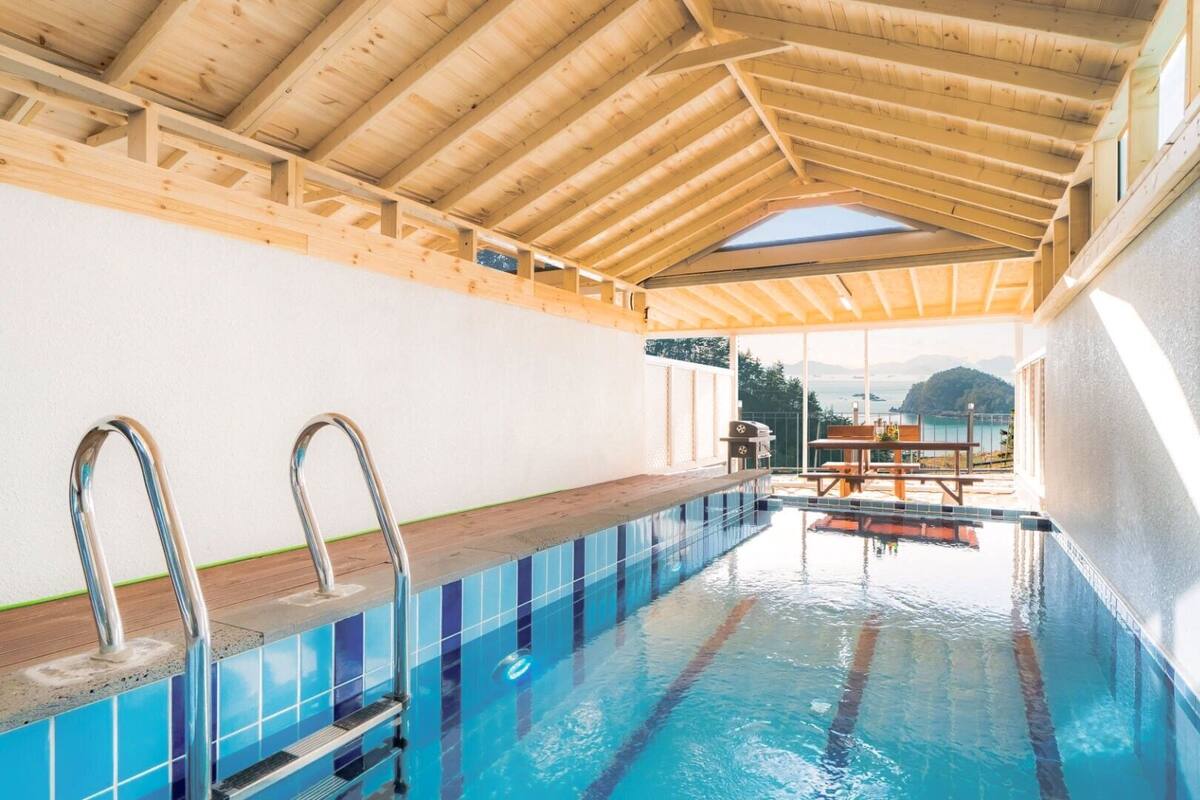 An indoor swimming pool with wooden beams, a diving board, and a view of mountains.