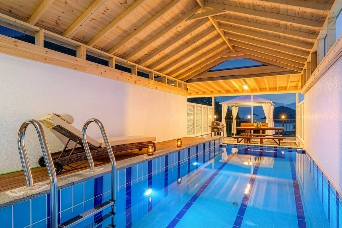 An indoor swimming pool with a wooden ceiling, a sunken bench, and a table with chairs.