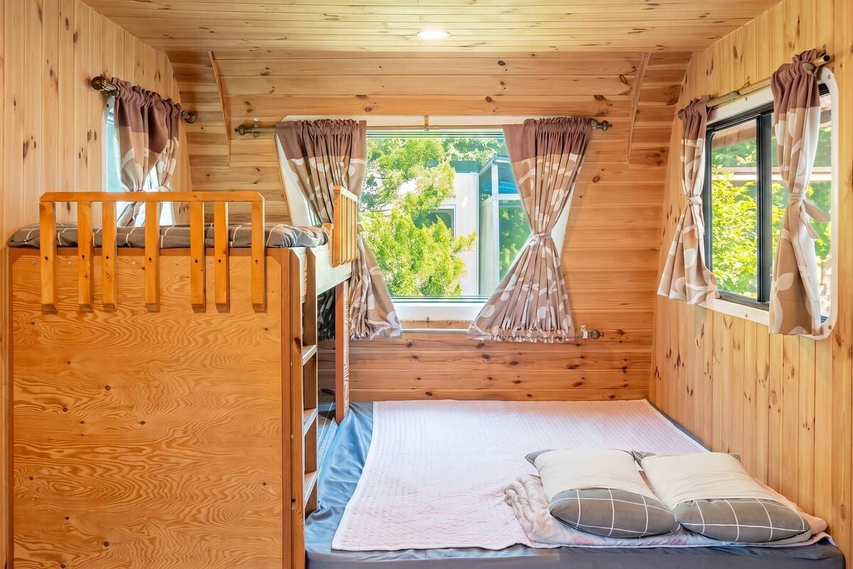 Ein Holzhütten-Zimmer mit Etagenbetten, einem Fenster mit Vorhängen und Blick auf grüne Natur.