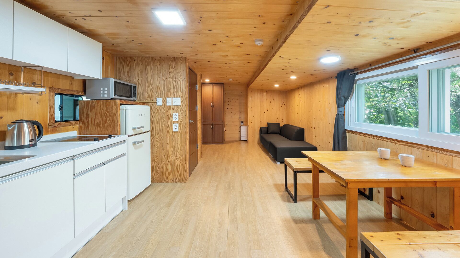 A compact kitchen with white cabinets, a microwave, and a kettle. There's a dining area with a table and chairs, and a sofa.
