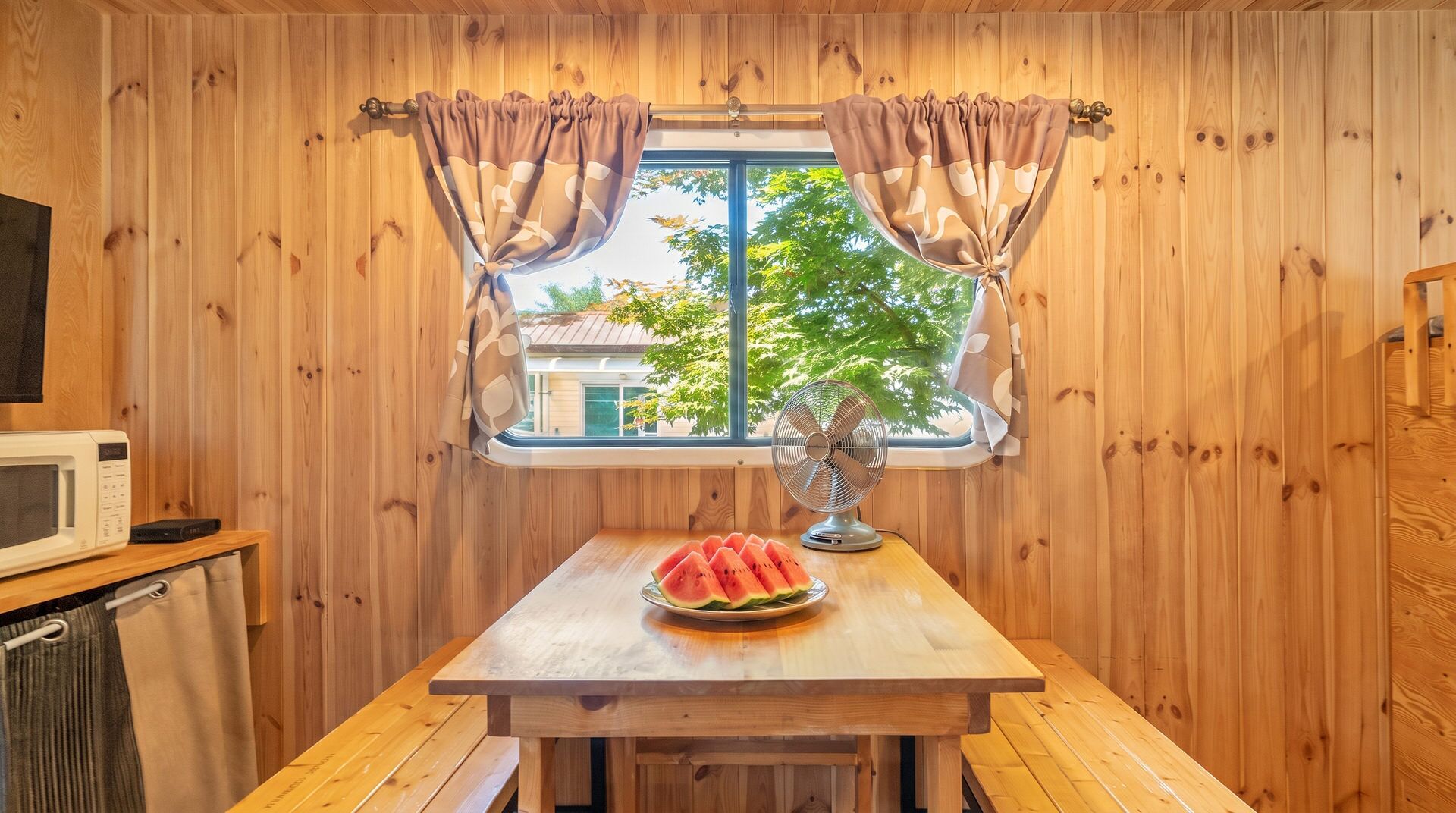 Quarto de cabana de madeira com uma mesa de madeira, micro-ondas e ventoinha.