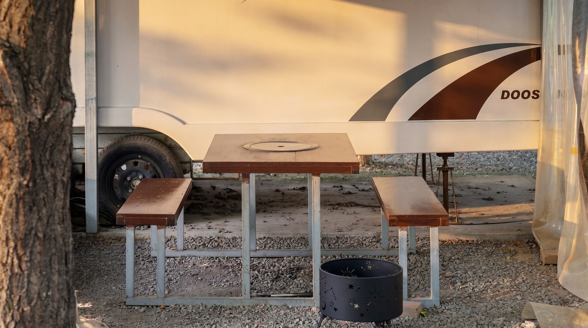 A portable table with two benches and a trash can, set up outdoors with a gravel ground.