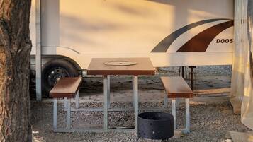 A portable table with two benches and a trash can, set up outdoors with a gravel ground.