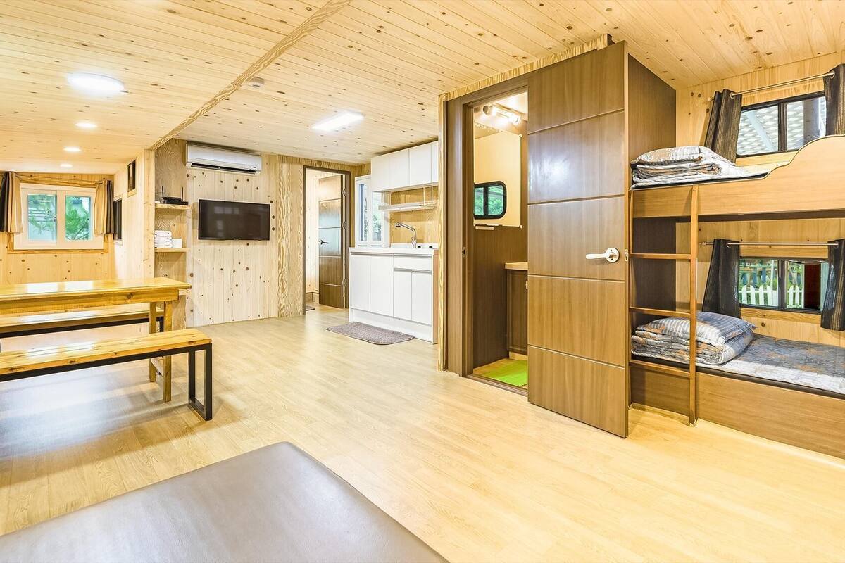Ein gemütlicher, holzgetäfelter Innenraum mit Küchenzeile, Essbereich und Schlafbereich inklusive Bett und Fenster.
