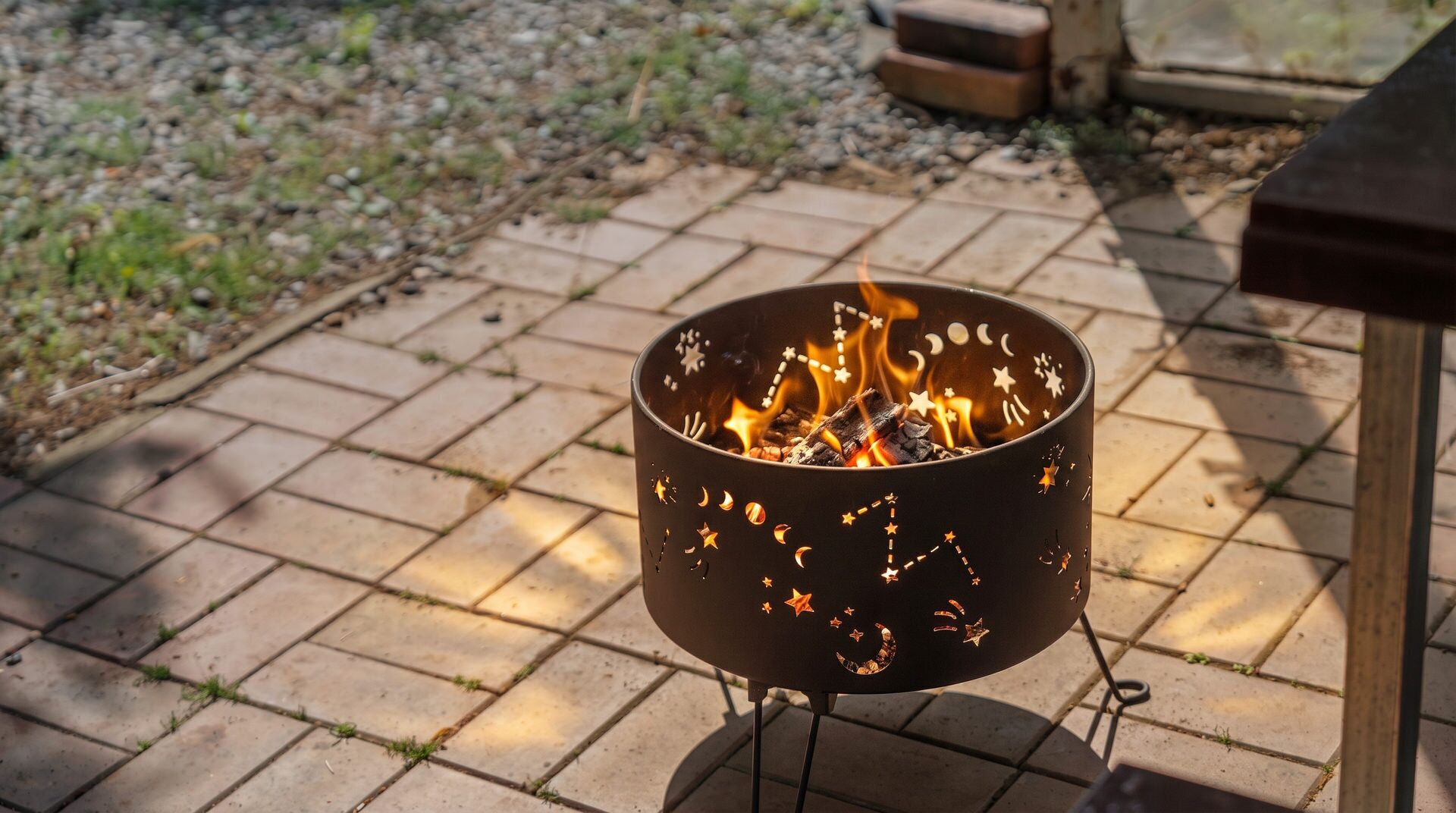 A metal fire pit with star and moon cutouts, placed on a brick patio.