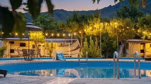 A swimming pool with a slide, surrounded by trees and string lights, with RVs in the background. - Gapeyong Donghwa Caravan (Gapyeong)