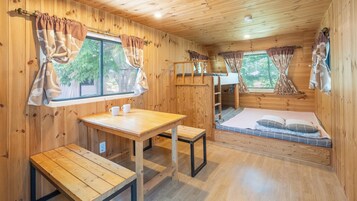 Interior de una cabaña con una mesa de madera, bancos, literas y cortinas.