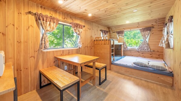 L’intérieur d’une cabane en bois, avec un lit superposé, une table en bois et des bancs.