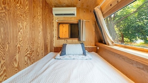 Un interior de madera con cama, ventana y unidad de aire acondicionado.