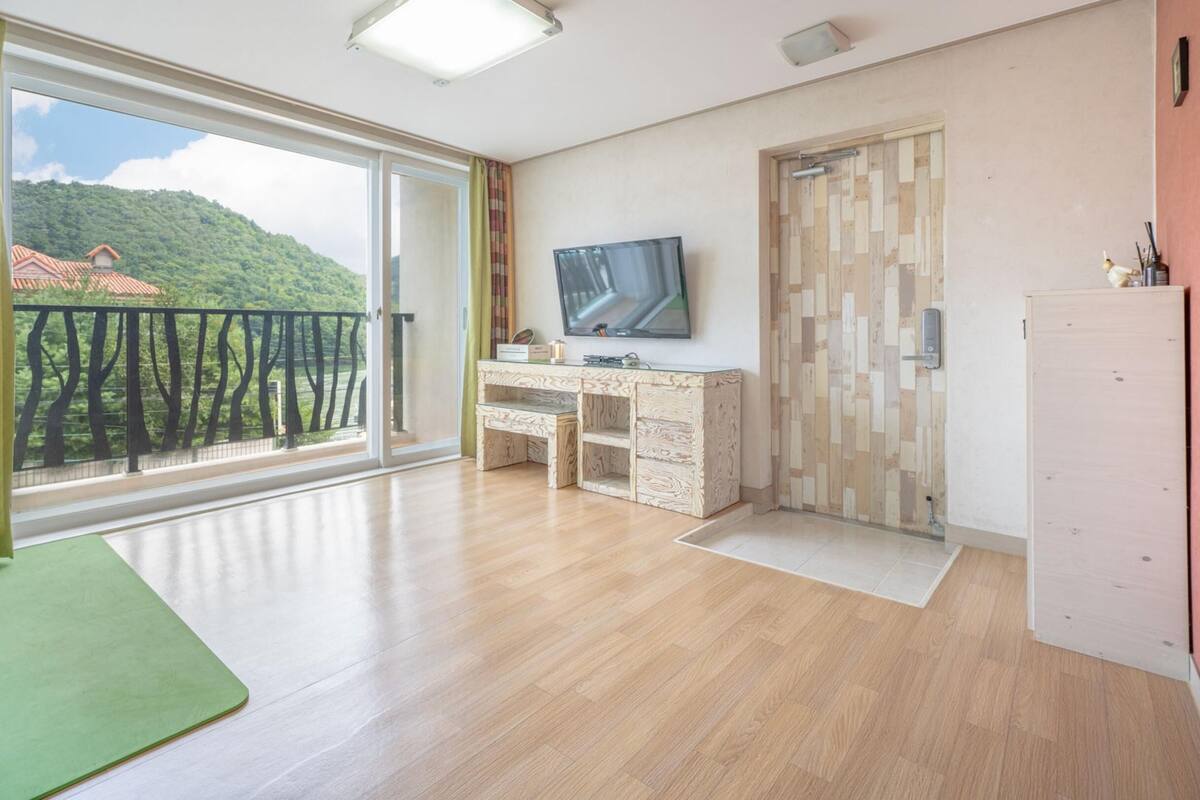 Een moderne kamer met een grote schuifglazen deur naar een balkon, een houten bureau met een flatscreen televisie en een houten kledingkast.