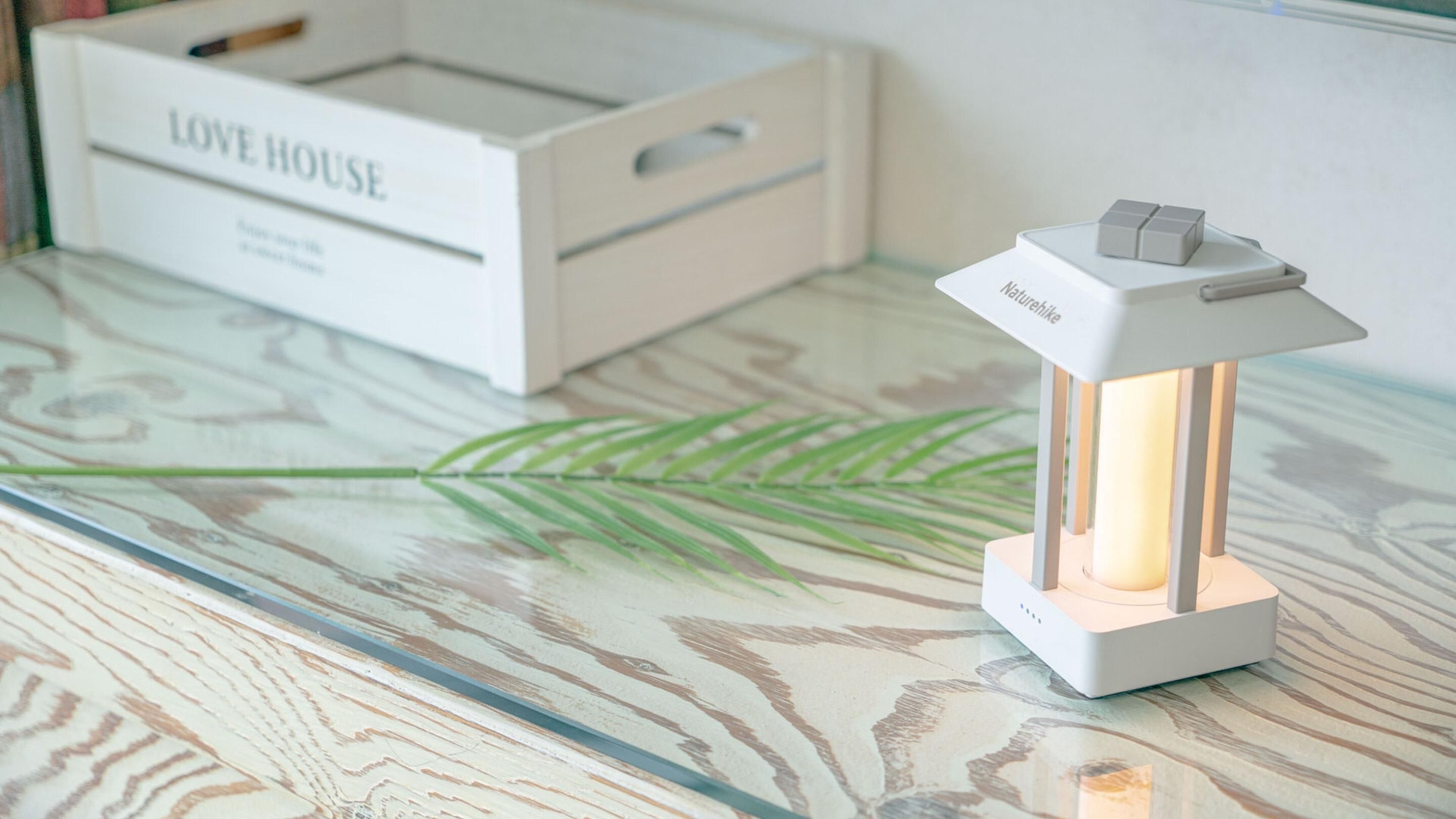 A white table lamp with a switch on top, placed on a glass table with a leaf pattern.