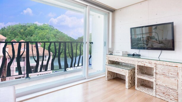 Een moderne woonkamer met een grote schuifpui naar een balkon, een flatscreen televisie aan de wand en een glazen salontafel.