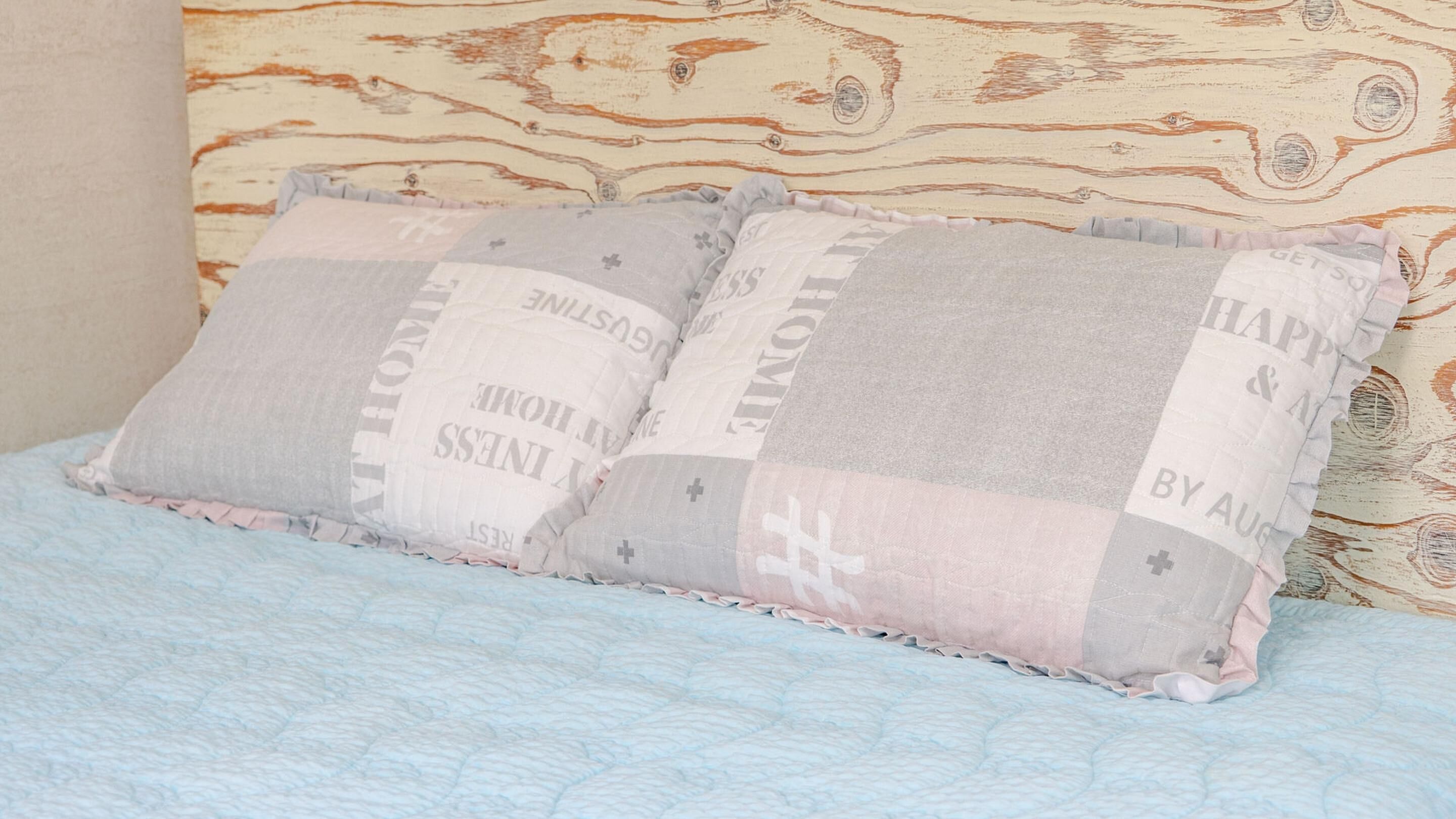 A bed with a light blue quilt and two pillows with a patchwork design.