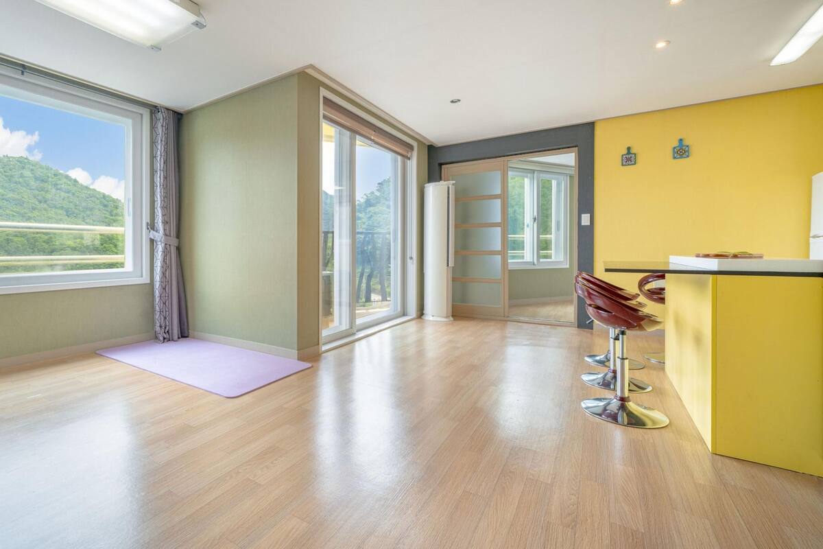 Ruime kamer met grote ramen, een yogamat, een bar en een glazen schuifdeur naar een balkon.