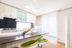 Een moderne keuken met witte kasten, een zwart aanrecht en groene barstoelen.