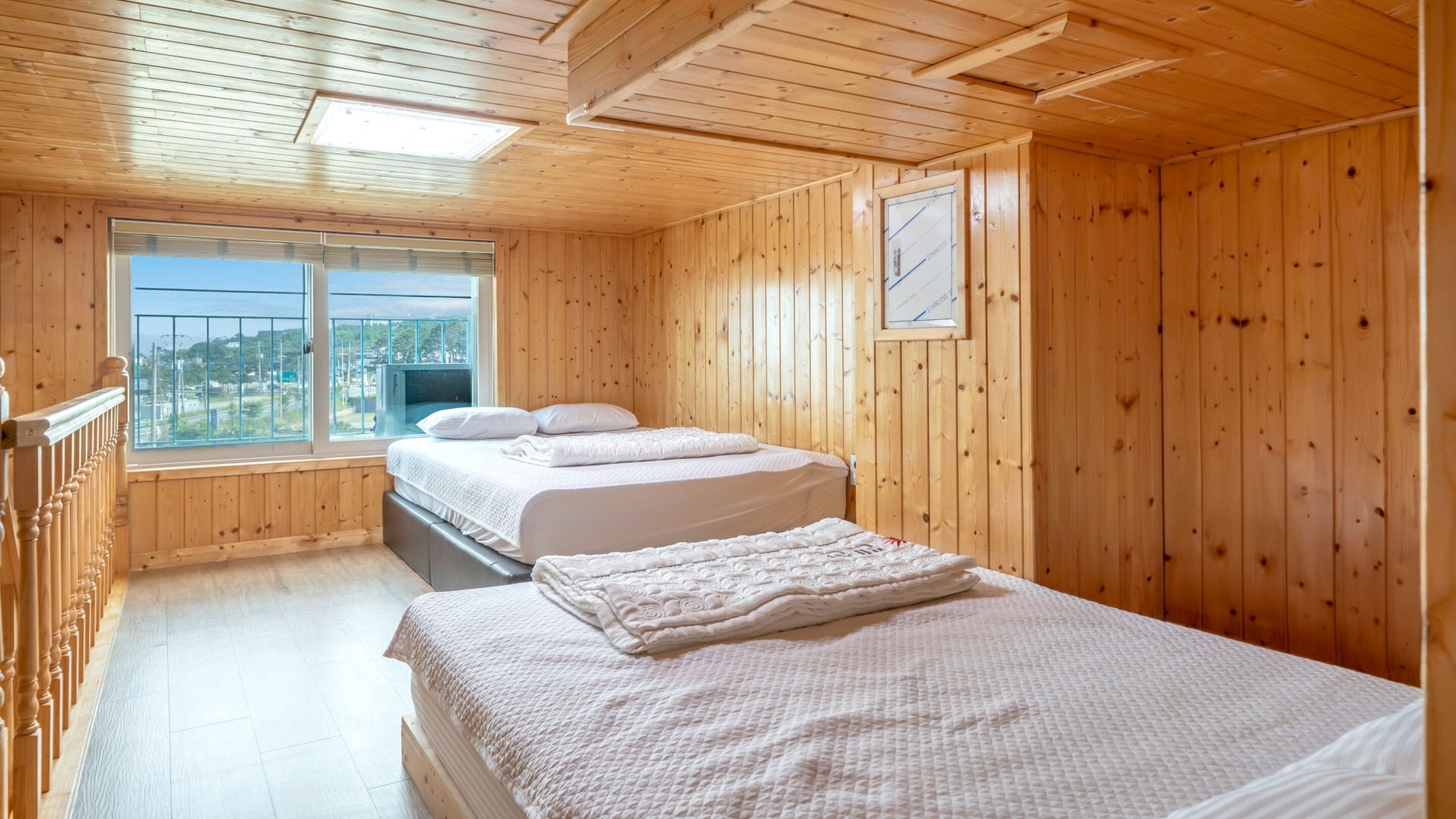 Una habitación con paneles de madera, dos camas, una ventana con vistas y un ventilador de techo.