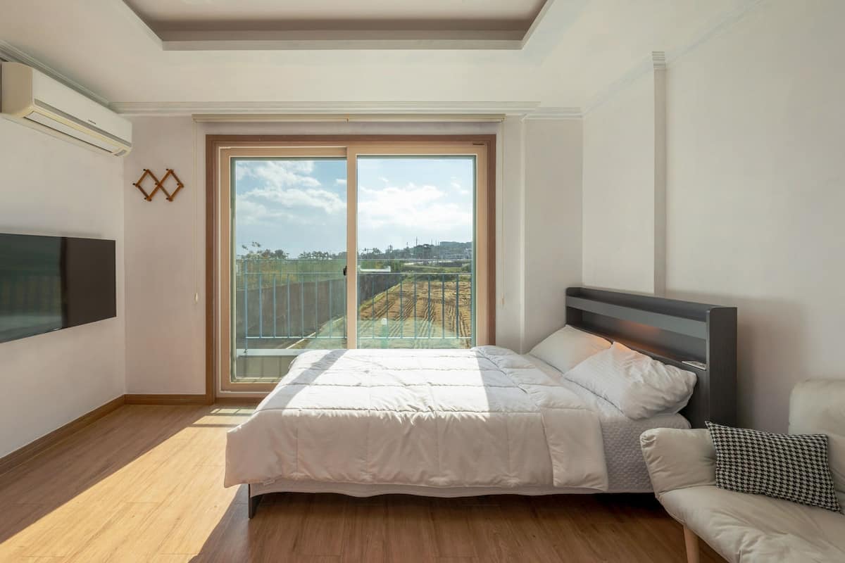 A bedroom with a bed, a TV, a sofa, and a large sliding glass door leading to an outdoor area.