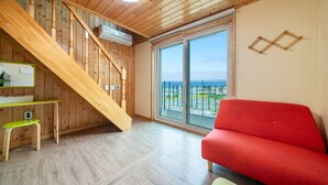 Une pièce avec un escalier en bois, un canapé rouge, une grande fenêtre donnant sur la mer et un plancher en bois.