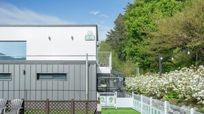 Een modern gebouw met een witte gevel, een balkon en een omheind tuingedeelte met witte bloemen.