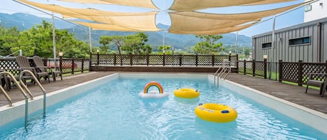 Piscina com boias flutuantes, uma cadeira de salva-vidas e vista para montanhas.