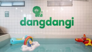 Ein Schwimmbeckenbereich mit einem großen, grünen Schild, auf dem 'dandangji' steht, und einem kleinen, grünen Logo darüber. Im Pool befinden sich aufblasbare Spielzeuge.