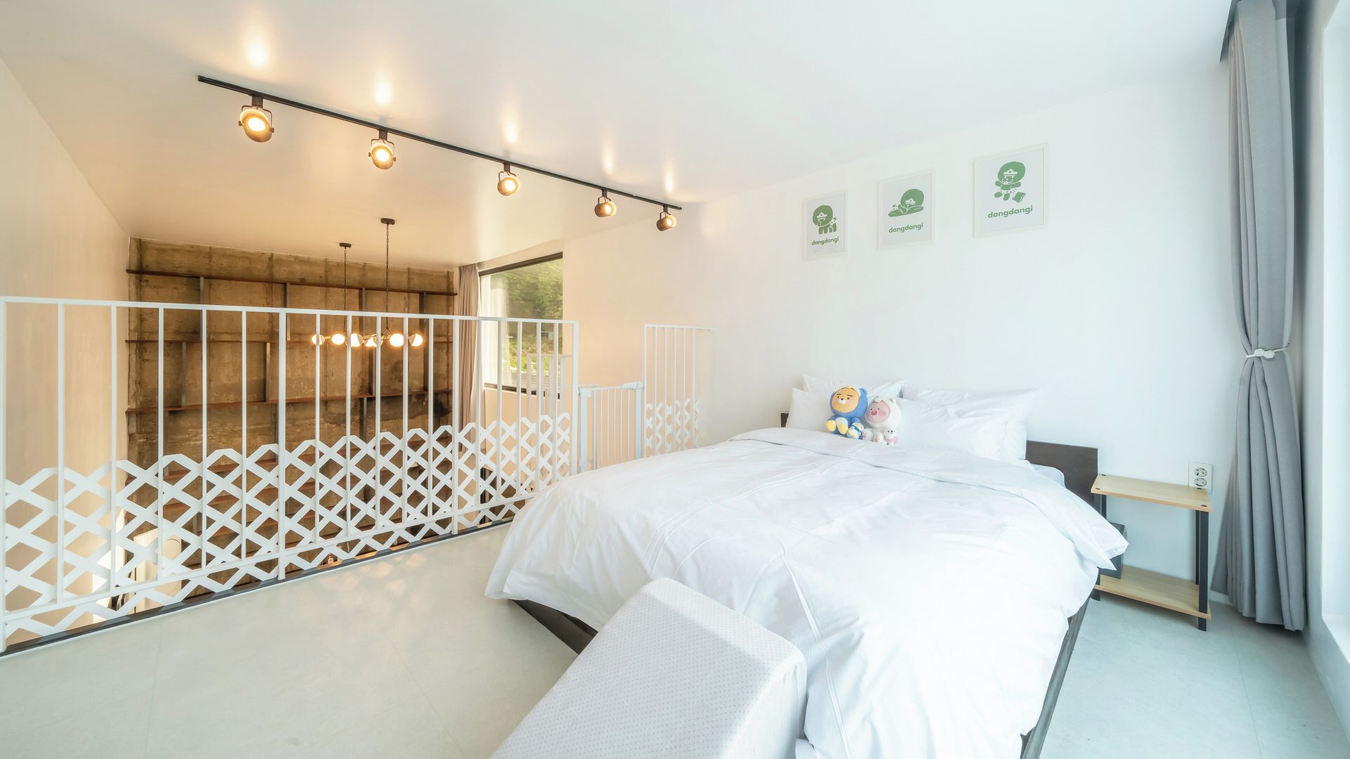 Un dormitorio moderno con cama, cortinas blancas, una mesita de noche y una pared decorativa con cuadros.