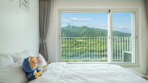 A hotel room with a bed, a window with a view of green hills, and a curtain. - Gapyeong Dangdangi Pet Poolvilla Blue (Gapyeong)