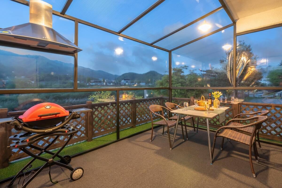 Une terrasse extérieure couverte, équipée d’un barbecue, de chaises en osier et d’une table dressée pour les repas.