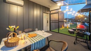 Een terras met een eettafel voor twee personen, rieten stoelen, een barbecue en uitzicht op de lucht.