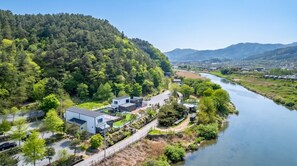 A residential area with modern houses, a river, and a forested hill. - Gapyeong Dangdangi Pet Poolvilla Blue (Gapyeong)